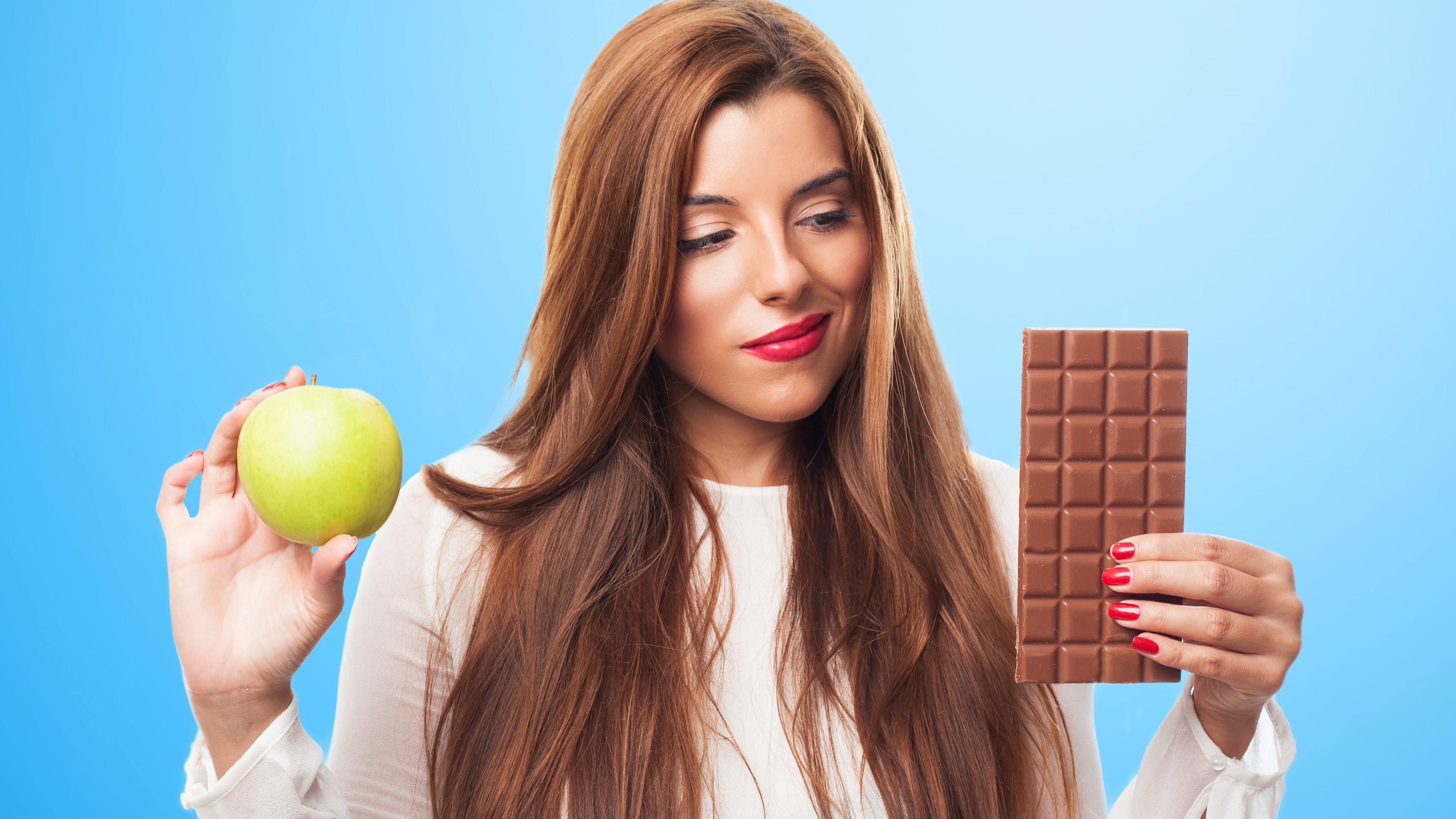 Девушка держит в руках яблоко и шоколадную плитку