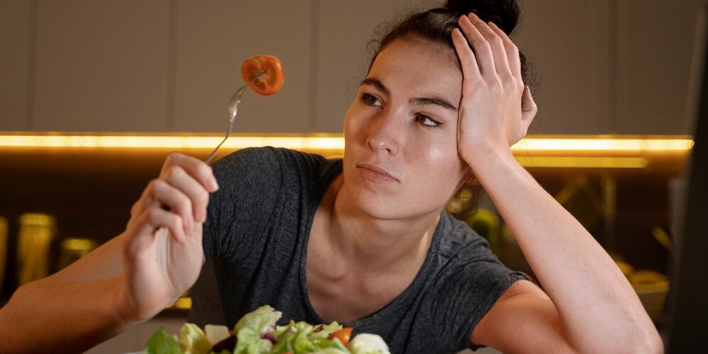 Женщина ест помидор с салатом