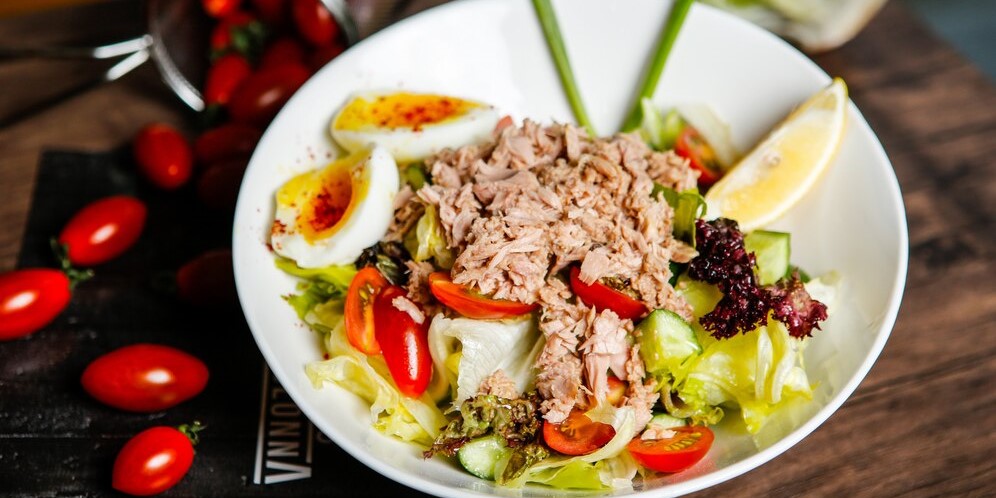 Салат из тунца с помидорами и вареным яйцом в тарелке с лимоном