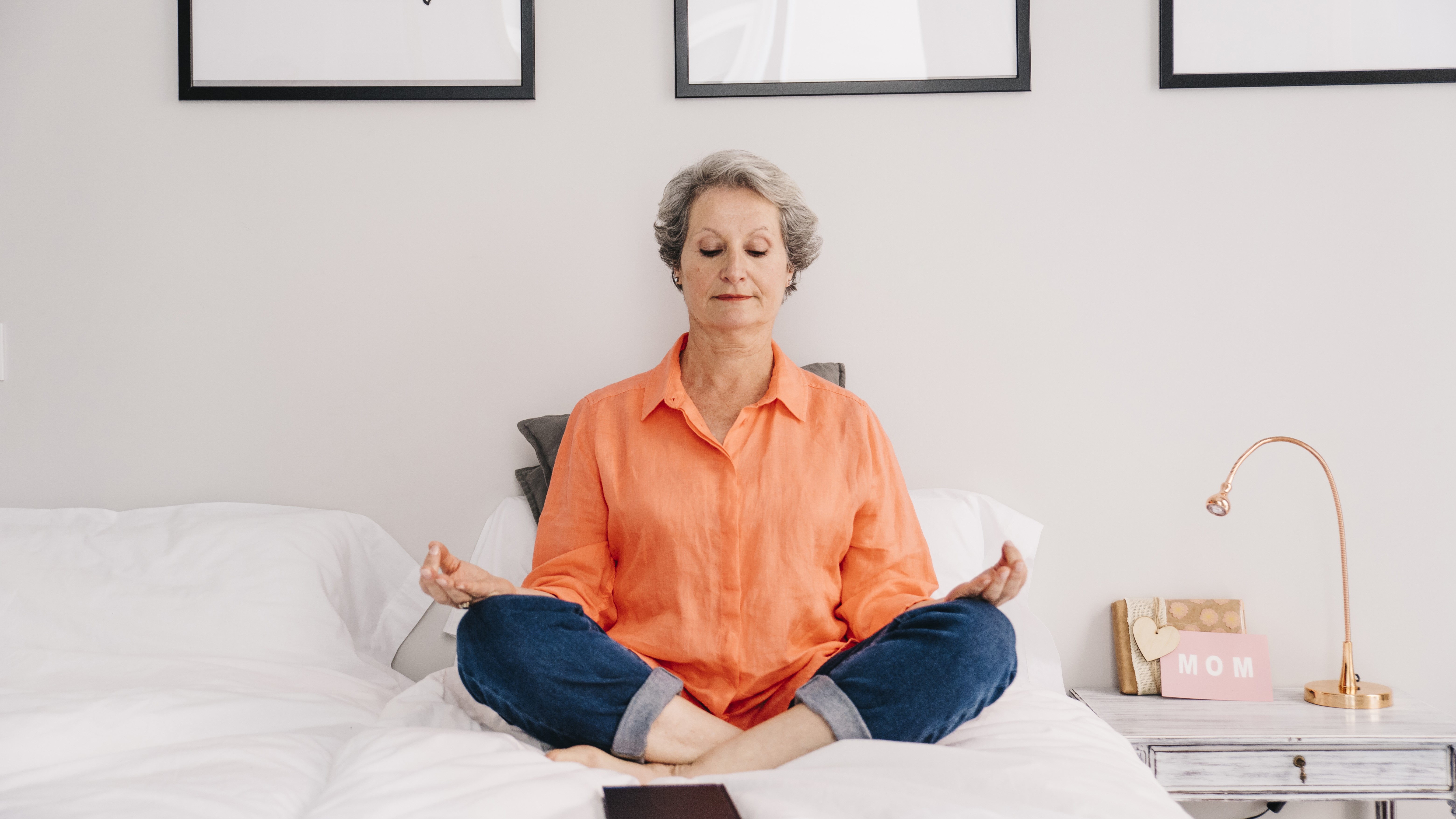 Пожилая женщина релаксирует на кровати в позе лотоса